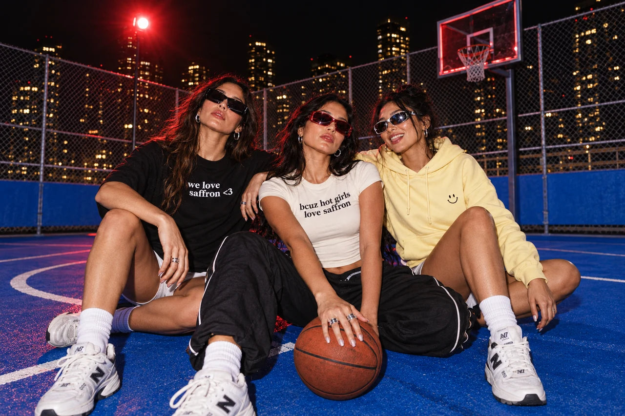Three adult friends wearing Saffron Club merch under rooftop lights